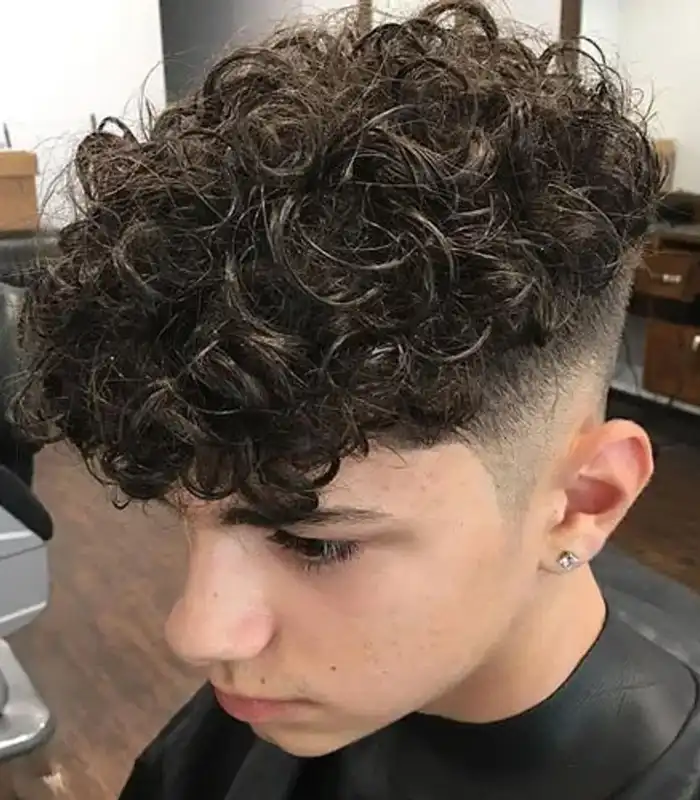 A young boy with naturally curly hair styled into a modern mullet, featuring short curls on the sides and longer, defined curls cascading down the back.