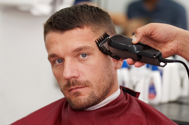 A barber uses electric clippers to give a man a Jason Statham-style buzz cut in a barbershop