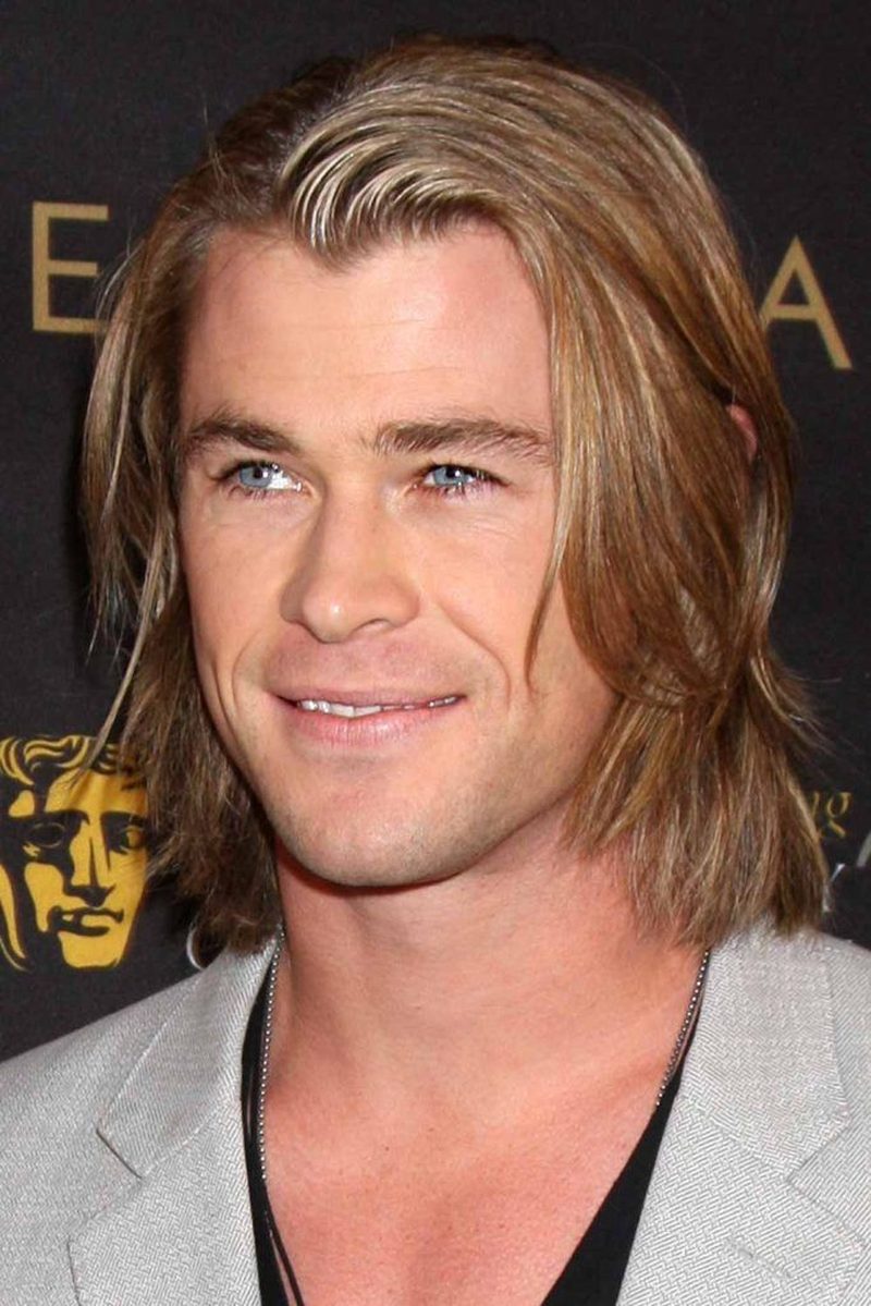Chris Hemsworth with medium-length wavy light brown hair styled in a sleek side-swept cut with textured layers and subtle highlights