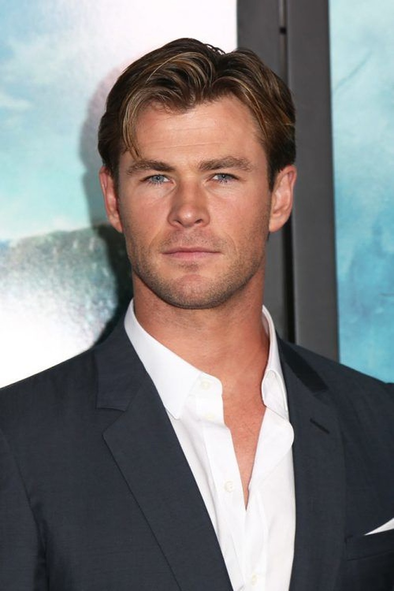 Chris Hemsworth with short medium-length brown hair in a textured swept-back cut with subtle highlights and a neat polished appearance