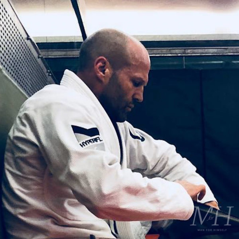 Jason Statham with a buzz cut and short facial hair, wearing a white Hyperfly gi
