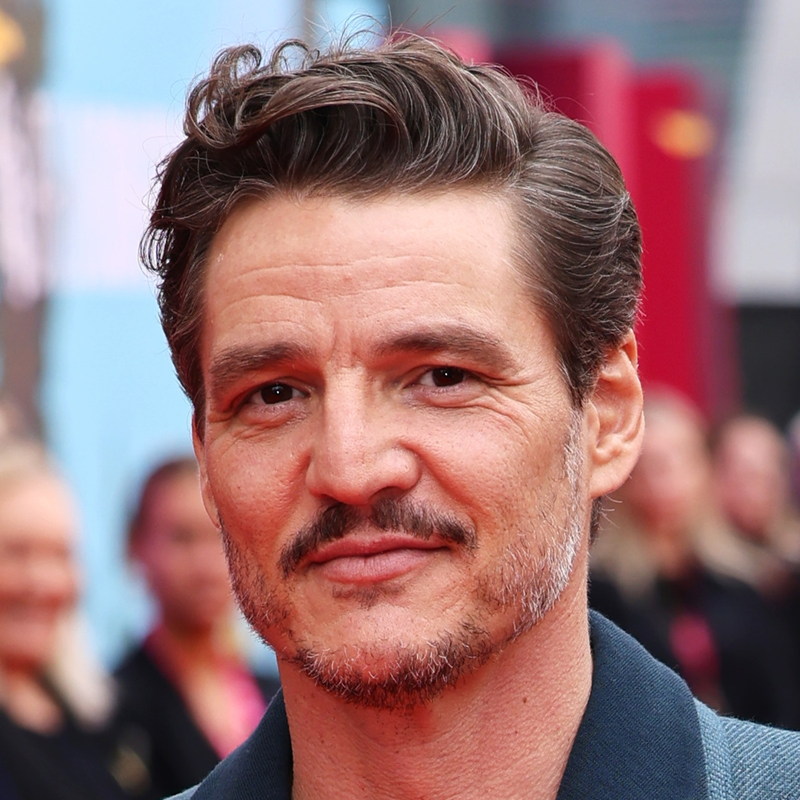 Pedro Pascal textured curly quiff hairstyle with short tapered fade sides showing thick wavy hair on top swept back with natural volume