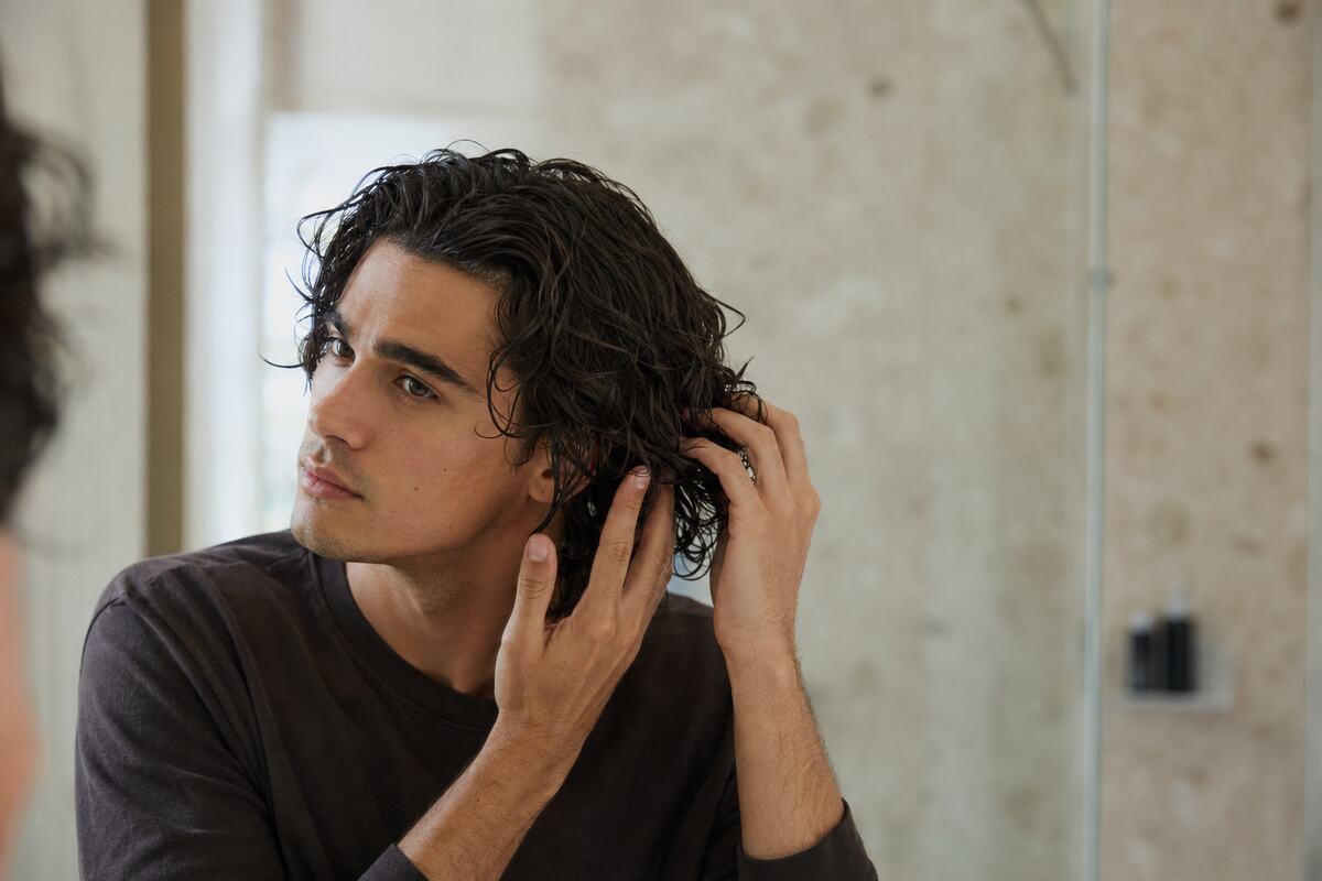 A fictional male model gently working lightweight curl cream through damp wavy hair.